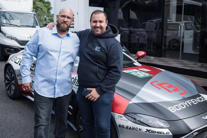 Rencontre devant une voiture de course aux couleurs de ses partenaires